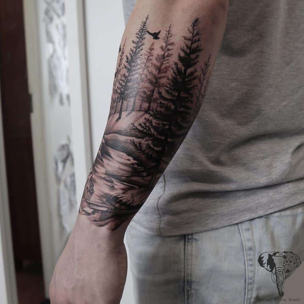 A person with a detailed forest landscape tattoo on their forearm, featuring tree silhouettes and a bird
