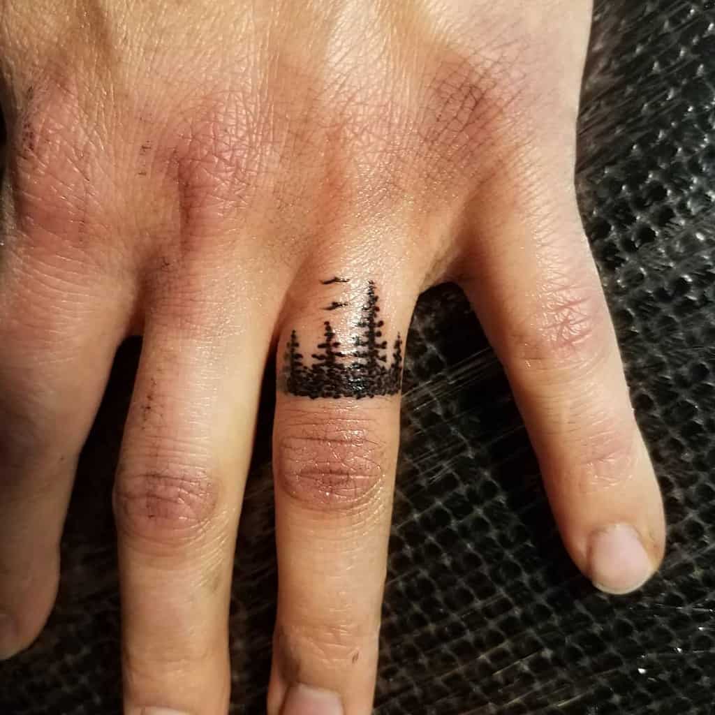 A black ink ring tattoo of a forest scene, featuring pine trees and birds