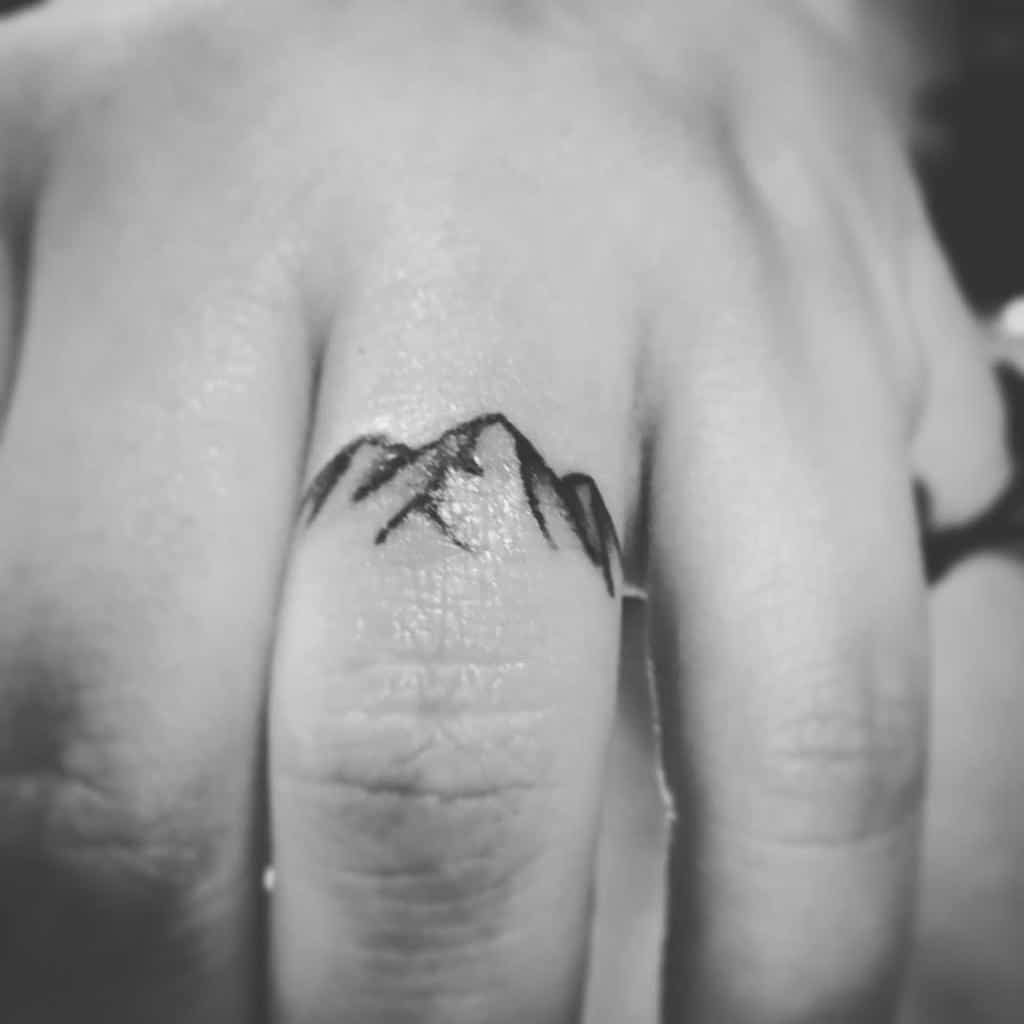 A minimalistic black ink ring tattoo of a mountain range