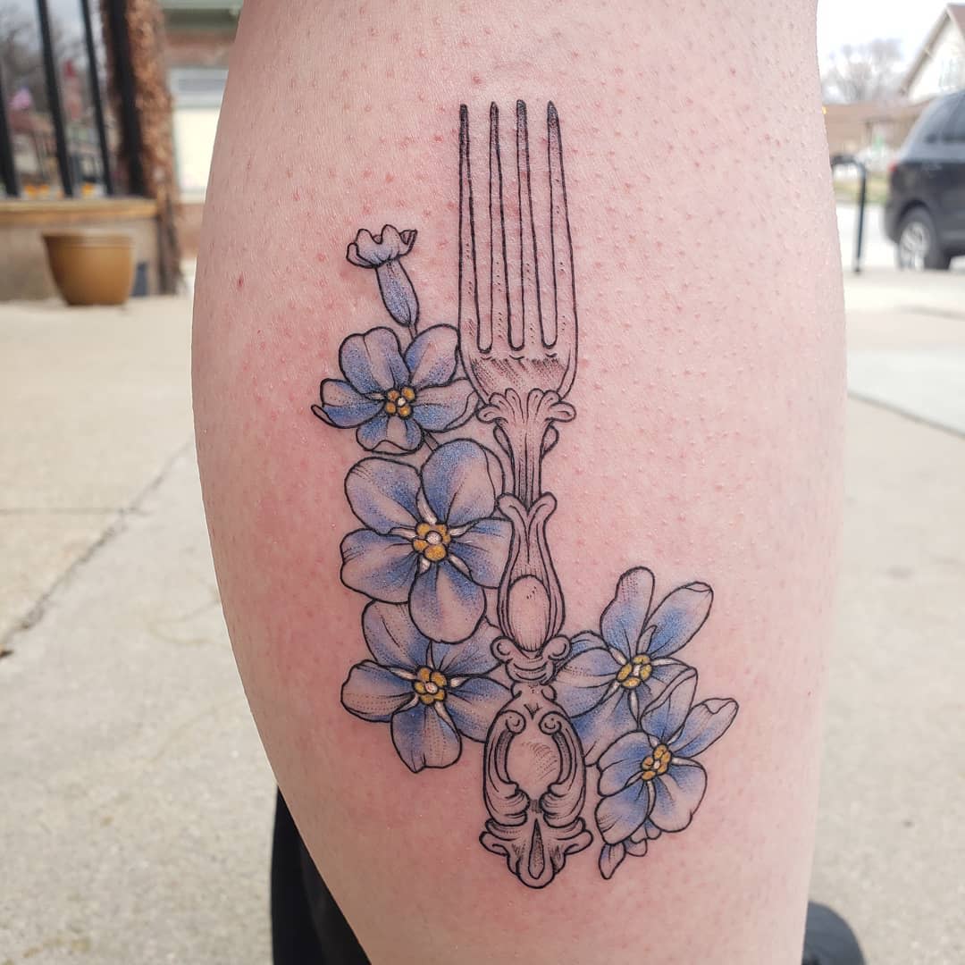 Tattoo of a vintage fork with blue flowers on a leg