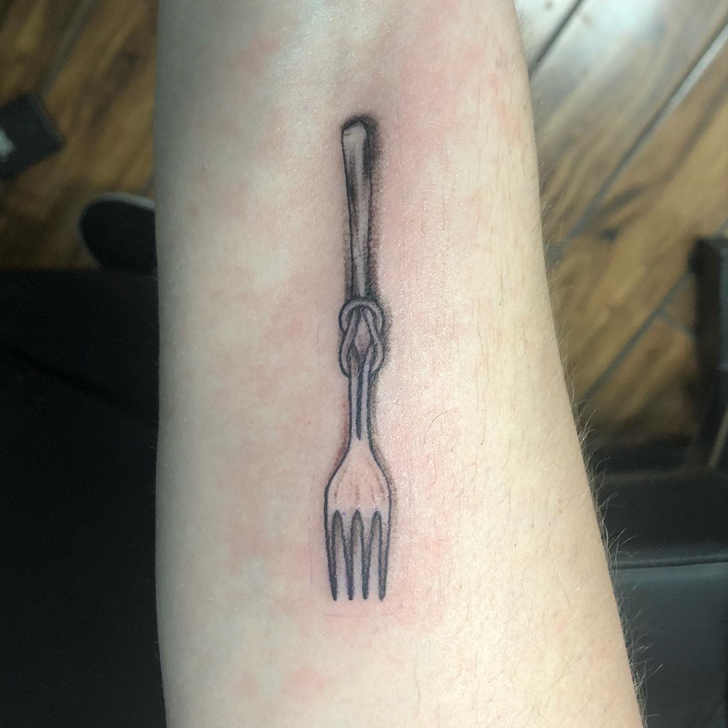 Tattoo of a fork with a knotted handle on a forearm