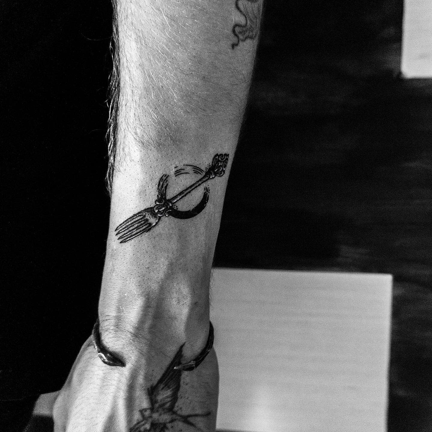 Forearm tattoo featuring a fork tied to a ring with a string