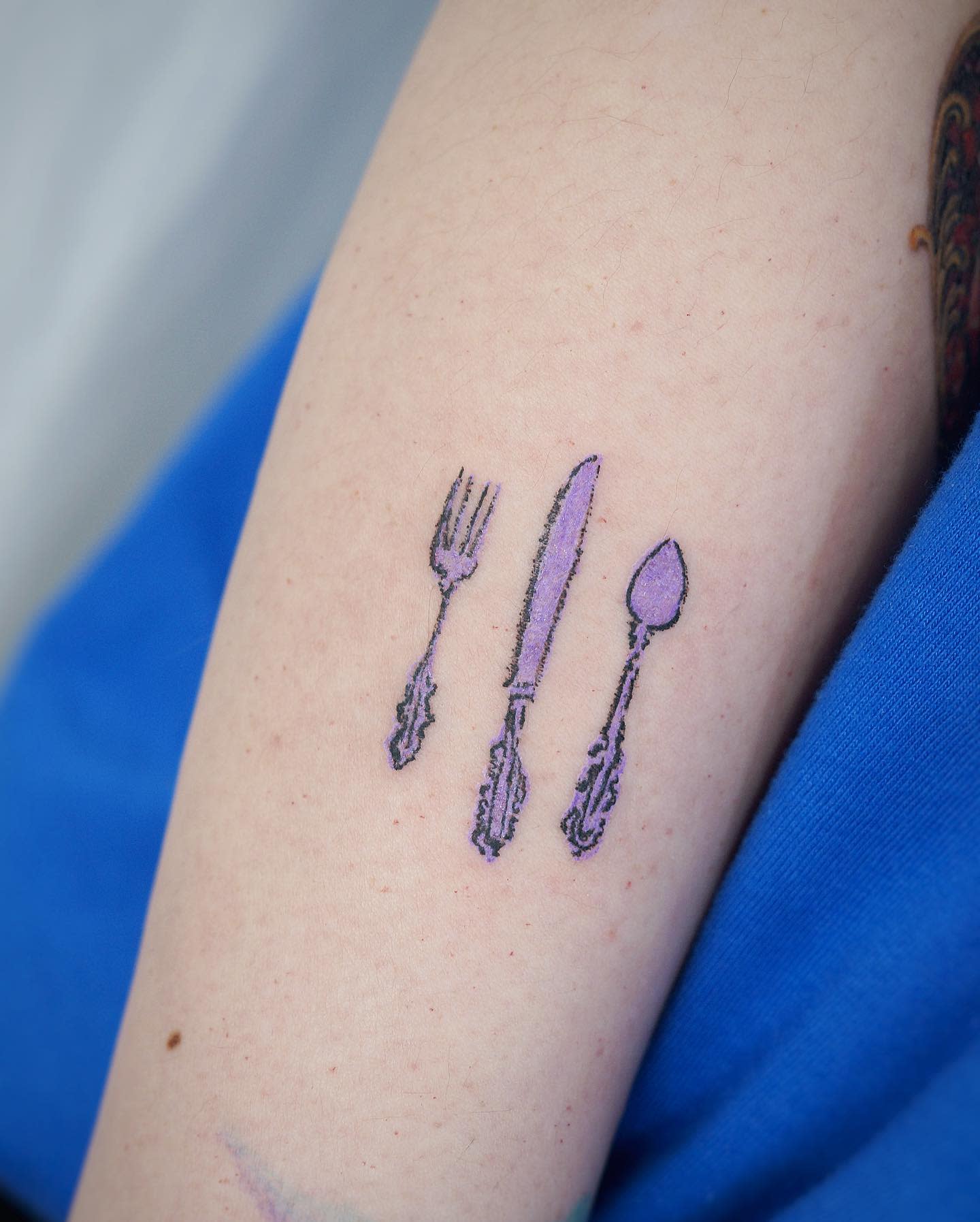 Tattoo of a fork, knife, and spoon on an arm