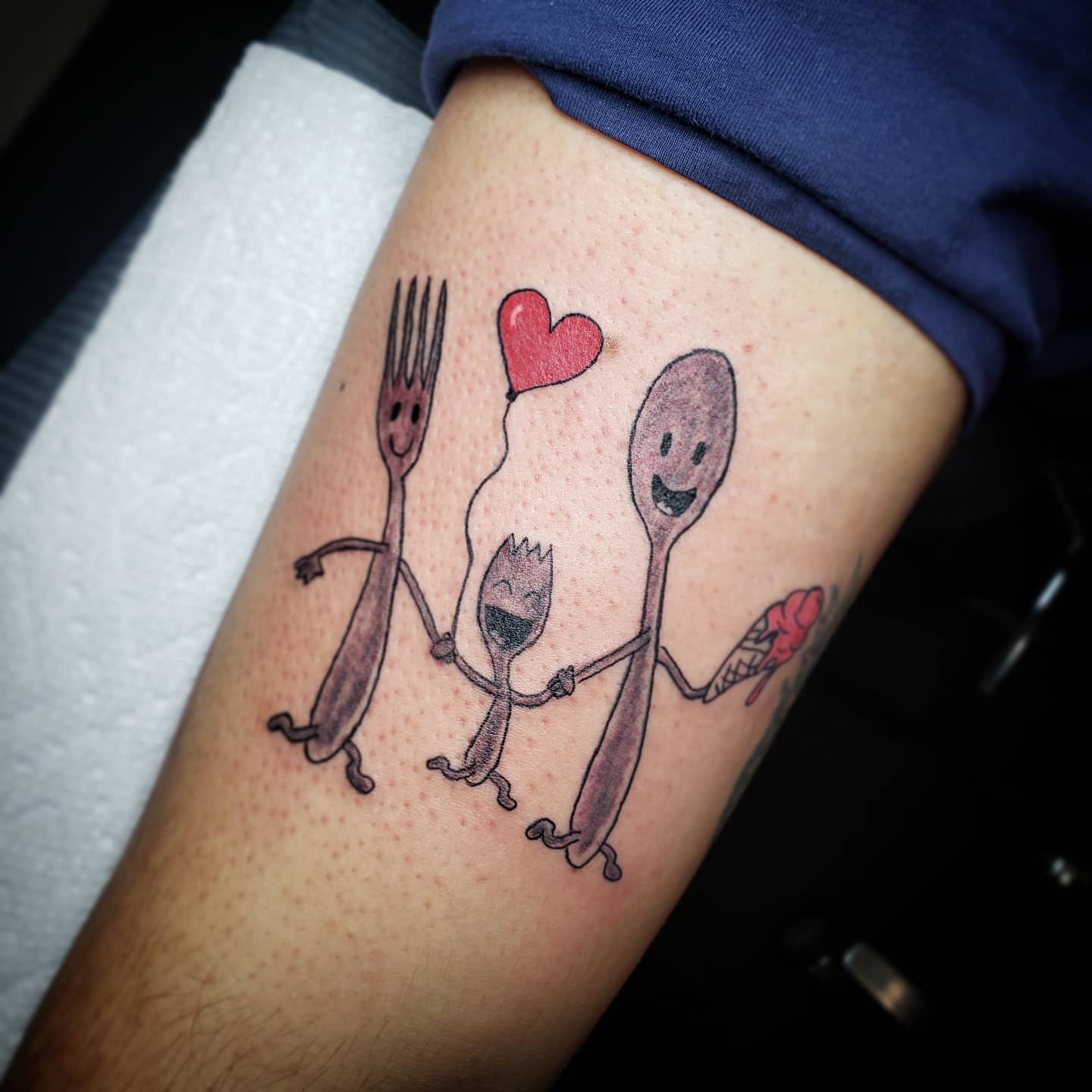 Tattoo of a happy fork, spoon, and spork holding hands; spoon holds an ice cream