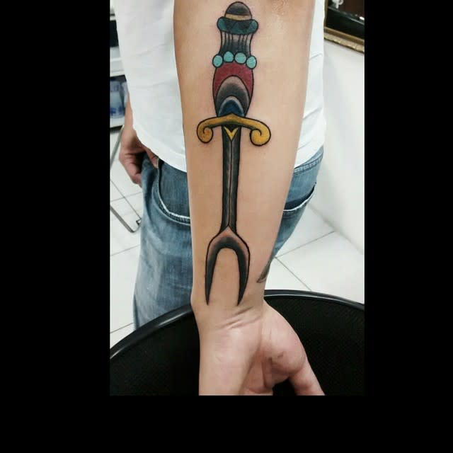 Forearm tattoo of a stylized dagger with detailed handle and colorful accents