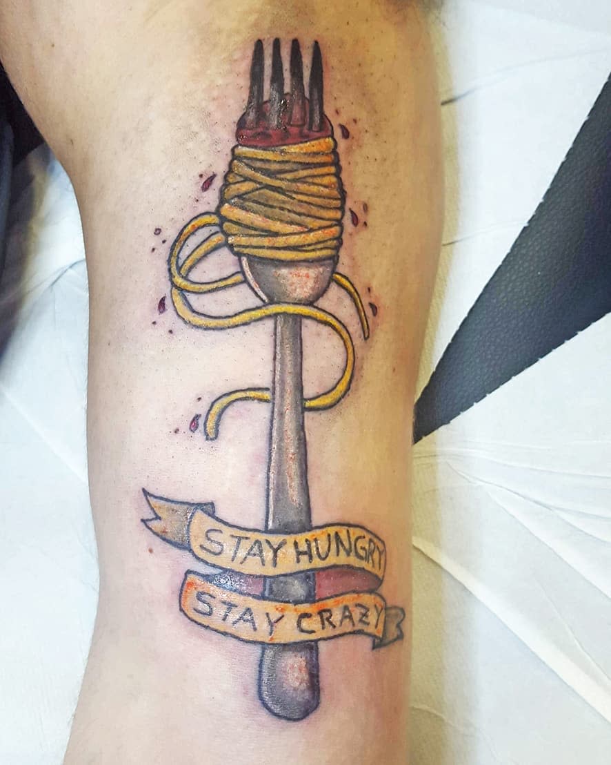Tattoo of a fork with spaghetti, with text "Stay Hungry, Stay Crazy" below it
