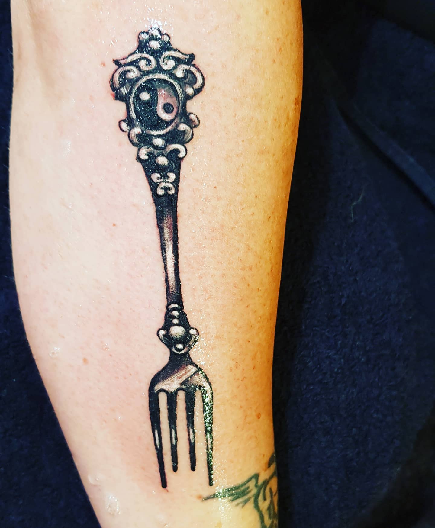 Intricate tattoo of a decorative fork with a yin-yang symbol on forearm