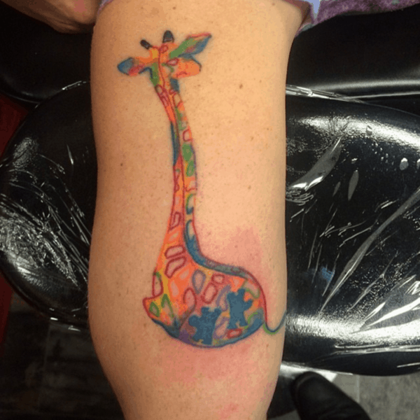 Full color arm tattoo of abstract, multi-colored, puzzle piece giraffe.