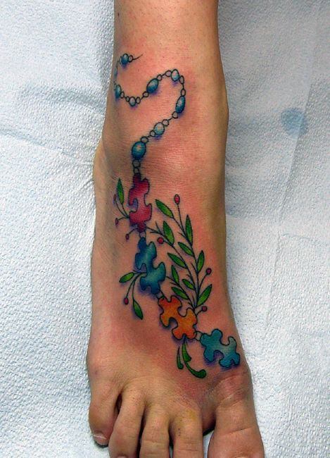 Full color foot tattoo of a chain of multi-colored puzzle pieces and beads with a tree branch.