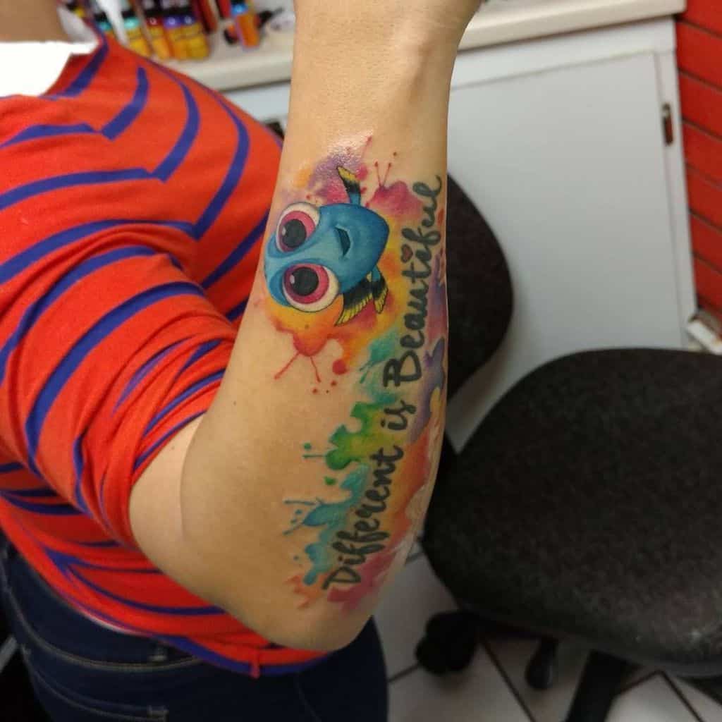 Full color forearm tattoo of “Dori” from Finding Nemo with watercolor splashes and inspirational quote.
