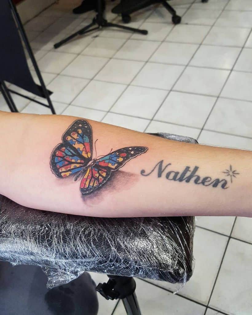 Full color forearm tattoo of a butterfly with Autism Awareness Puzzle wings and text: Nathen.