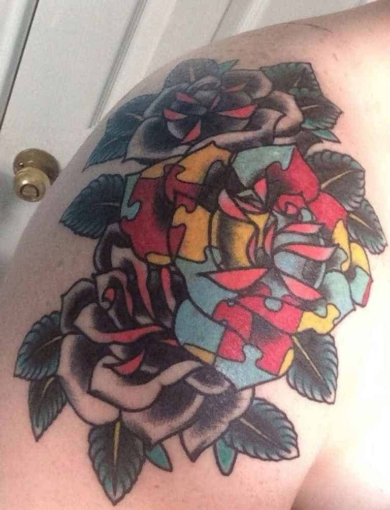 Full color shoulder tattoo of two black roses and one multi-colored puzzle piece rose.