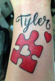 Full color tattoo of a red puzzle piece with a negative space heart and cursive script “Tyler”.