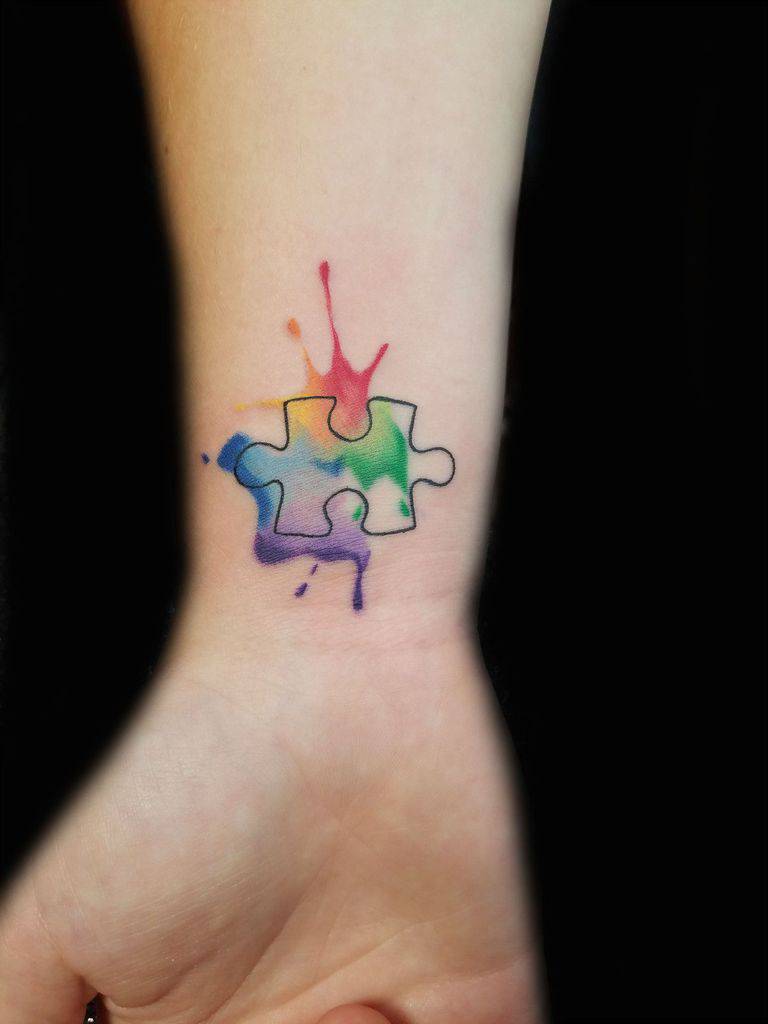 Full color wrist tattoo of watercolor splashes and line work puzzle piece.