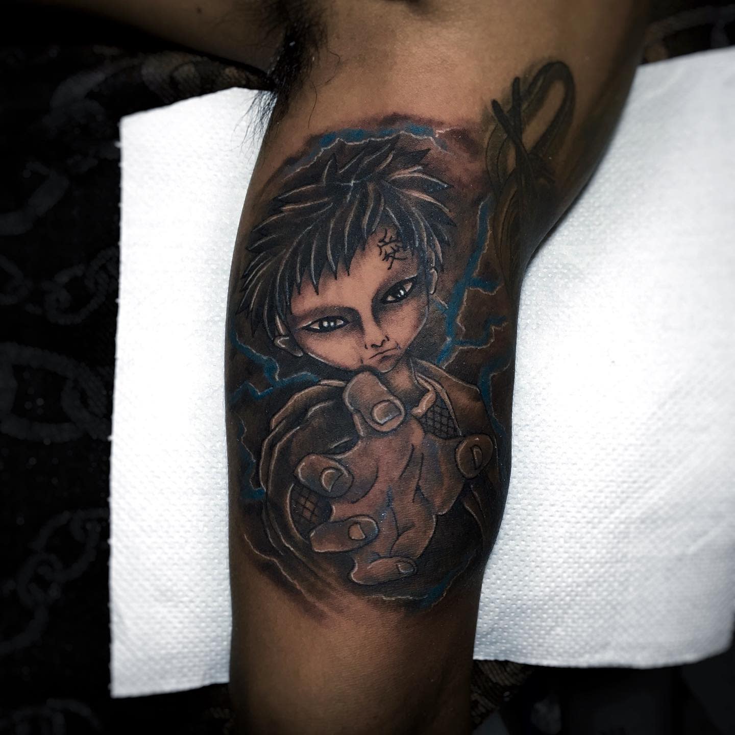 Tattoo of Gaara with outstretched hand and fierce expression on a muscular forearm
