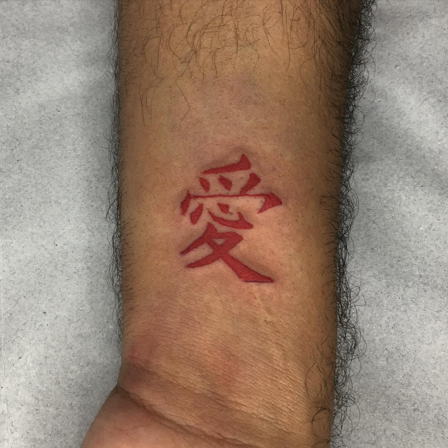 Forearm with red Chinese character tattoo symbolizing "love"