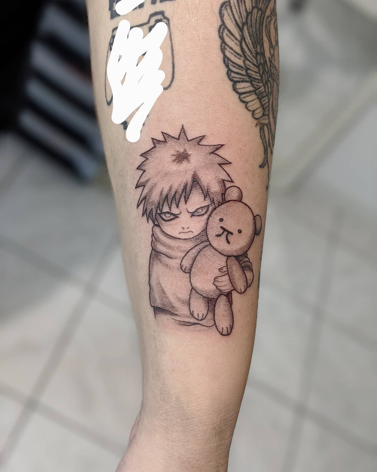 Tattoo of young Gaara with spiky hair holding a teddy bear on the inner arm
