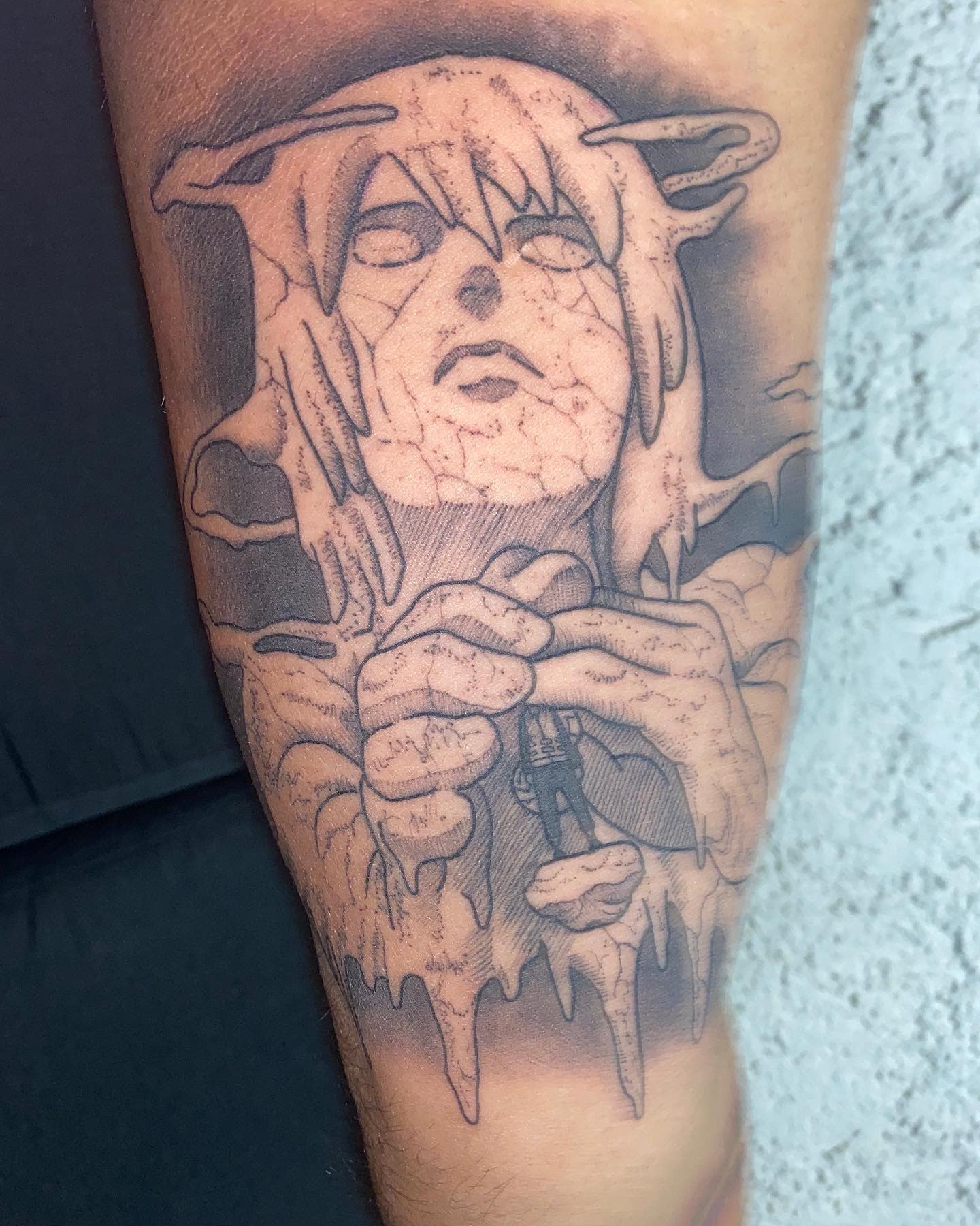 Tattoo of an eerie figure with cracked skin and long hair holding a small dangling individual