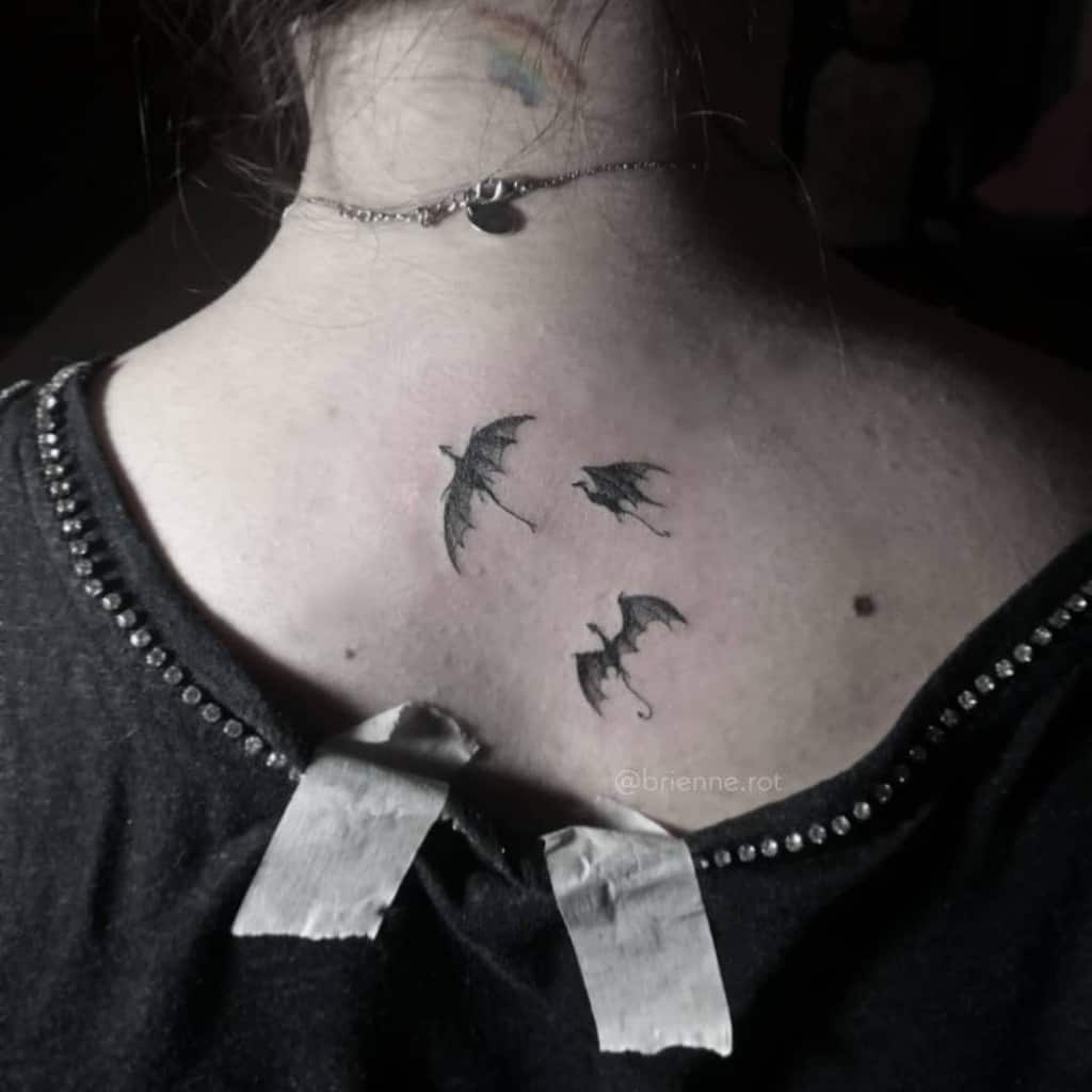 Minimalist black dragon tattoo on the upper back with three dragons flying together