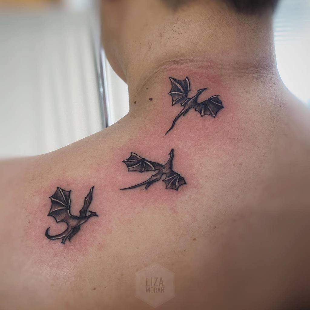 Back tattoo of three small black dragons in flight, symbolizing the dragons from Game of Thrones on the upper shoulder