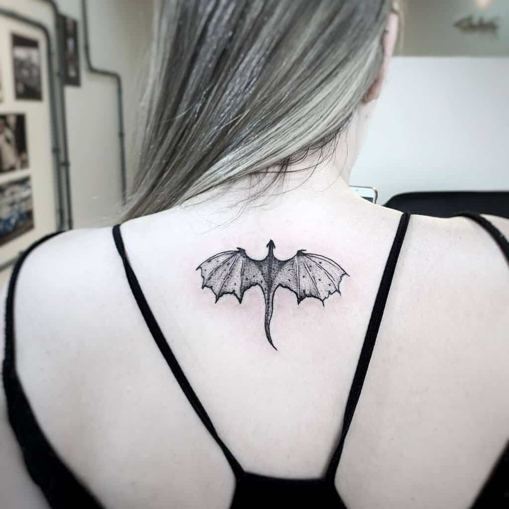 Minimalist dragon tattoo centered on the upper back, inspired by Game of Thrones, featuring detailed wings in black ink