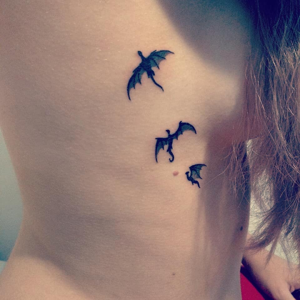 Small rib tattoo of three black dragons in flight, inspired by Game of Thrones, symbolizing Daenerys's dragons