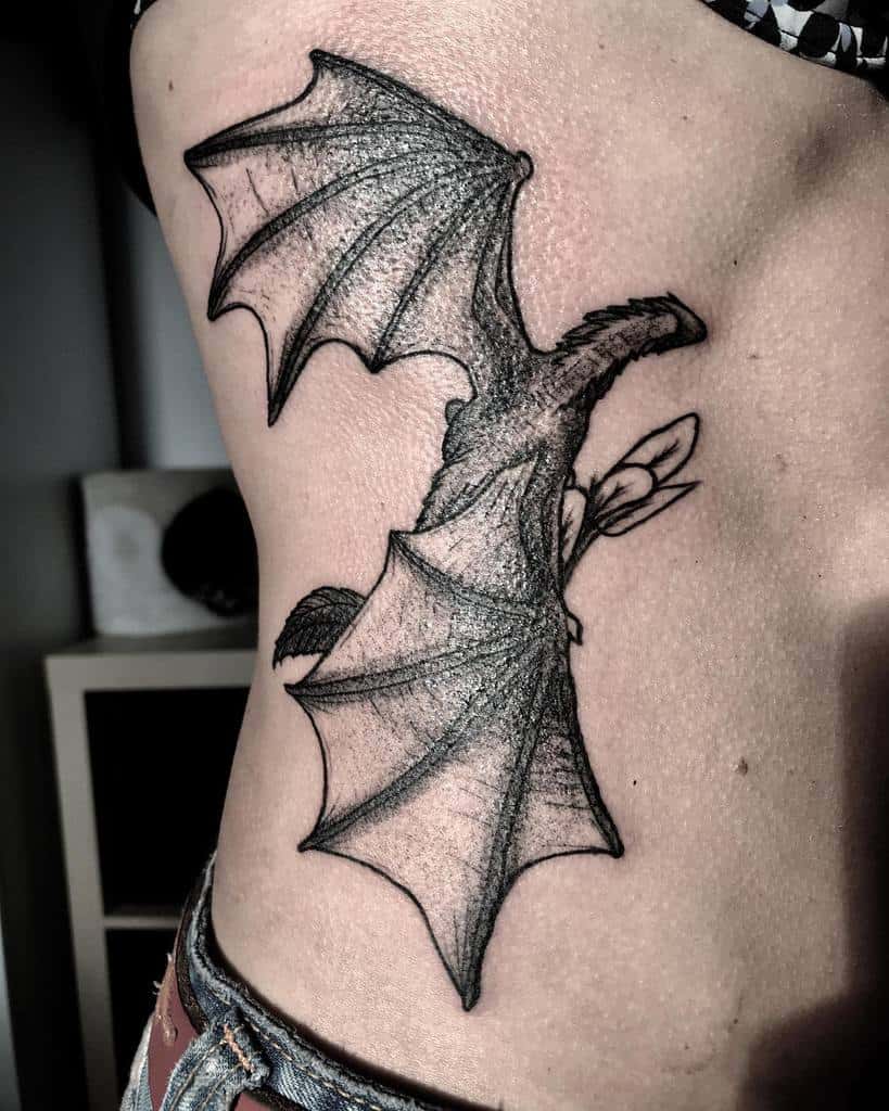 Detailed rib tattoo of a dragon with large textured wings, inspired by Game of Thrones, covering the side of the torso