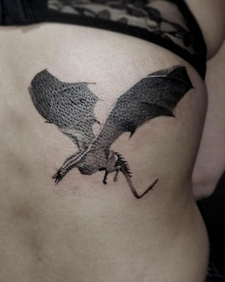 Black ink rib tattoo of a flying dragon with outstretched wings, inspired by Game of Thrones, featuring textured detailing