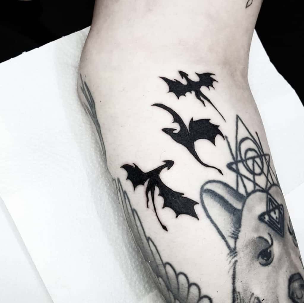 Black tattoos of three flying dragons