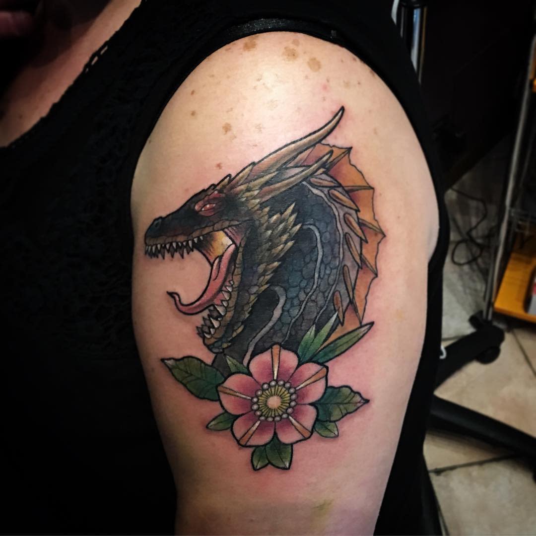 Arm tattoo of a roaring dragon above a pink flower with green leaves