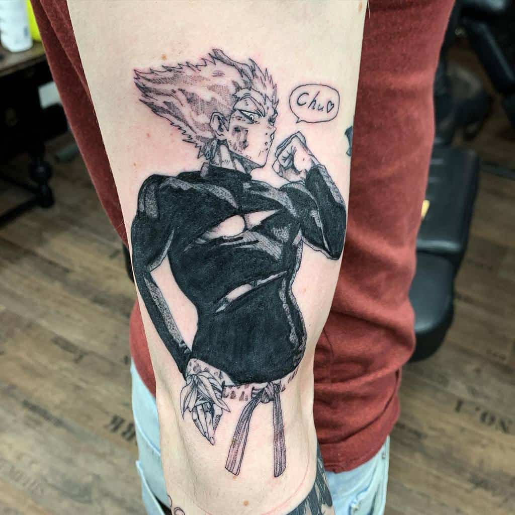 A black ink tattoo of Garou from One Punch Man in a confident pose, with battle scars and a speech bubble saying "Chu ♥"