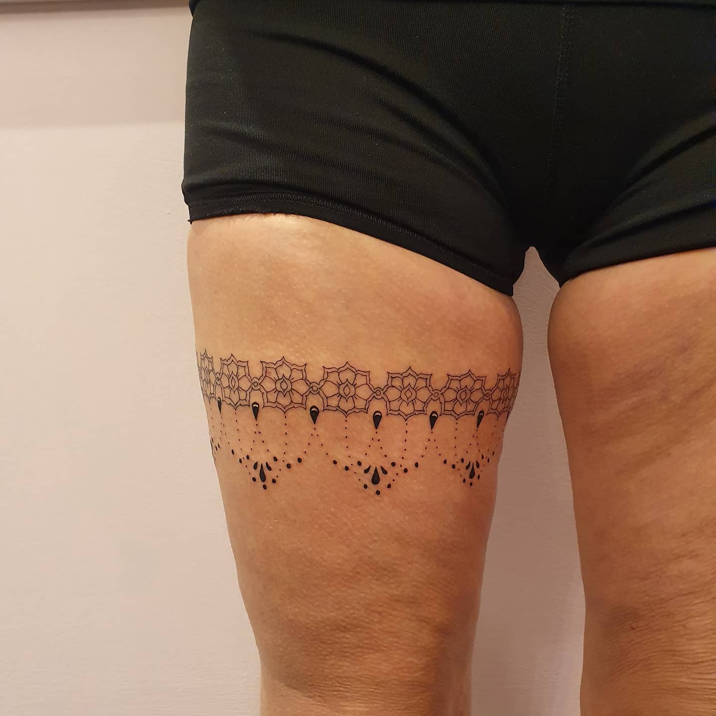 A lace garter tattoo encircles the upper thigh