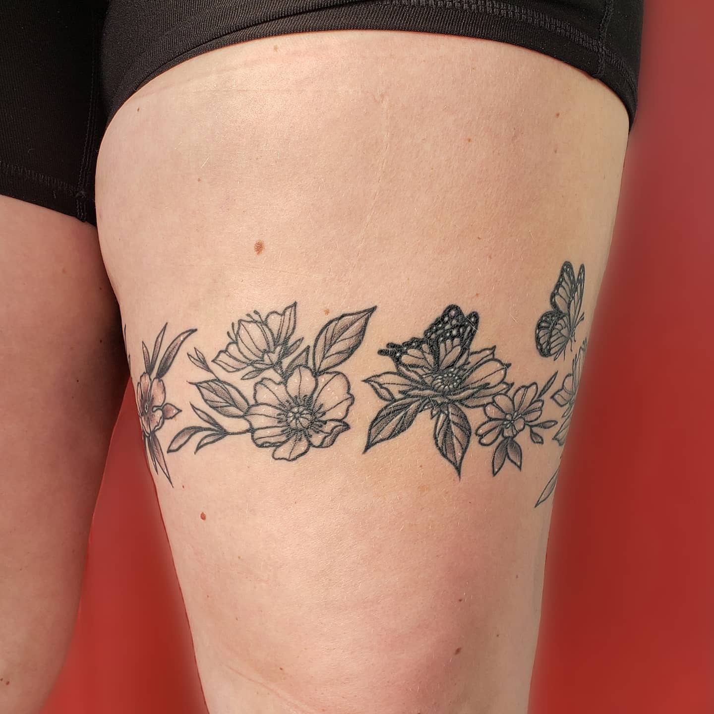Tattoo on thigh featuring black ink flowers and butterflies