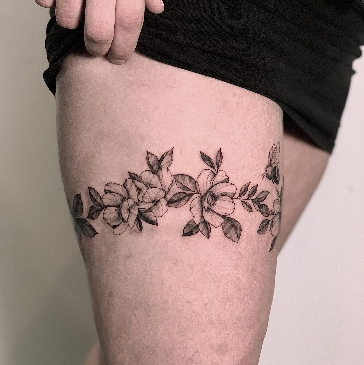 A thigh tattoo showcasing delicate flowers and leaves in black ink on fair skin