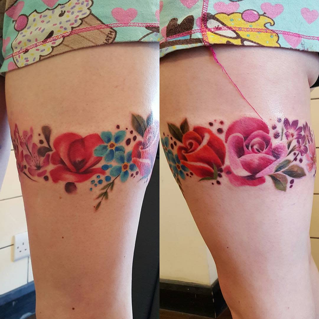 Colorful floral tattoo featuring roses and other flowers on a thigh