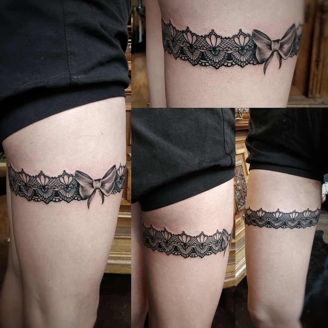 Black lace garter tattoo with a bow on individual’s thigh