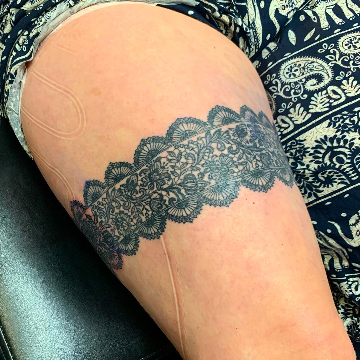 A detailed garter lace tattoo wraps around a thigh