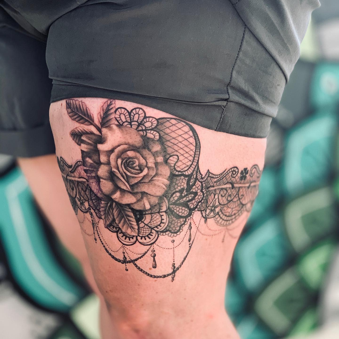 Tattoo on thigh features intricate lace pattern centered around a large shaded rose