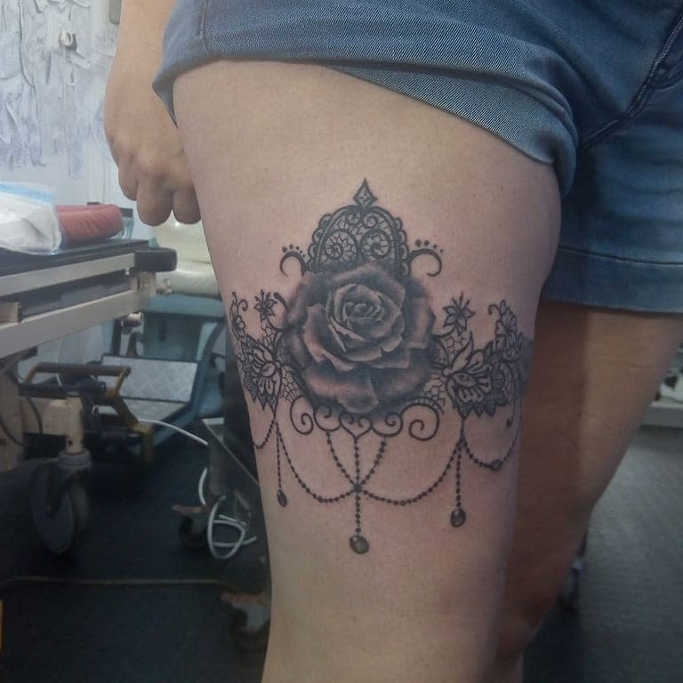 A leg tattoo of a rose surrounded by intricate designs and beads shown on an upper thigh