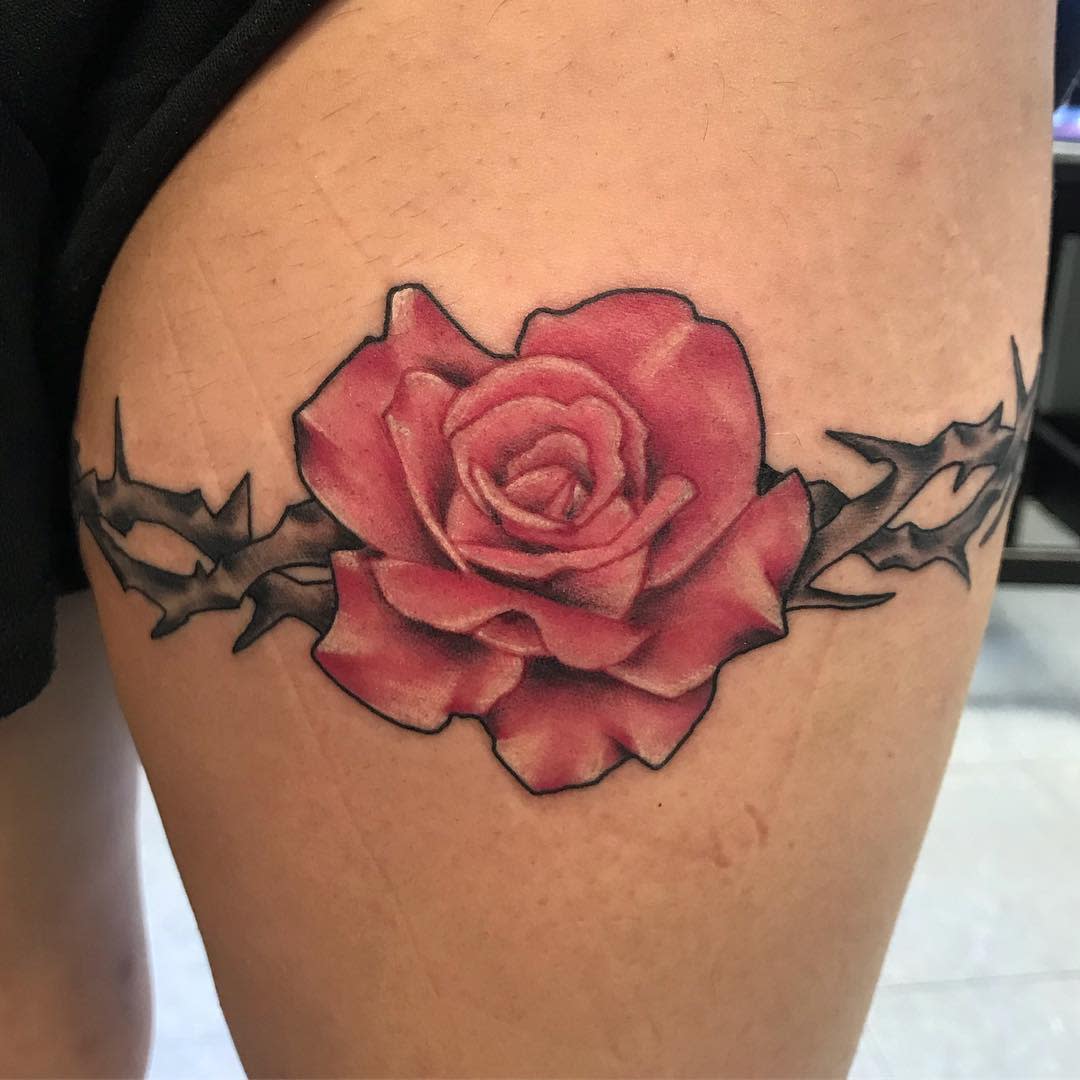 A tattoo featuring a pink rose with black thorns on the upper thigh