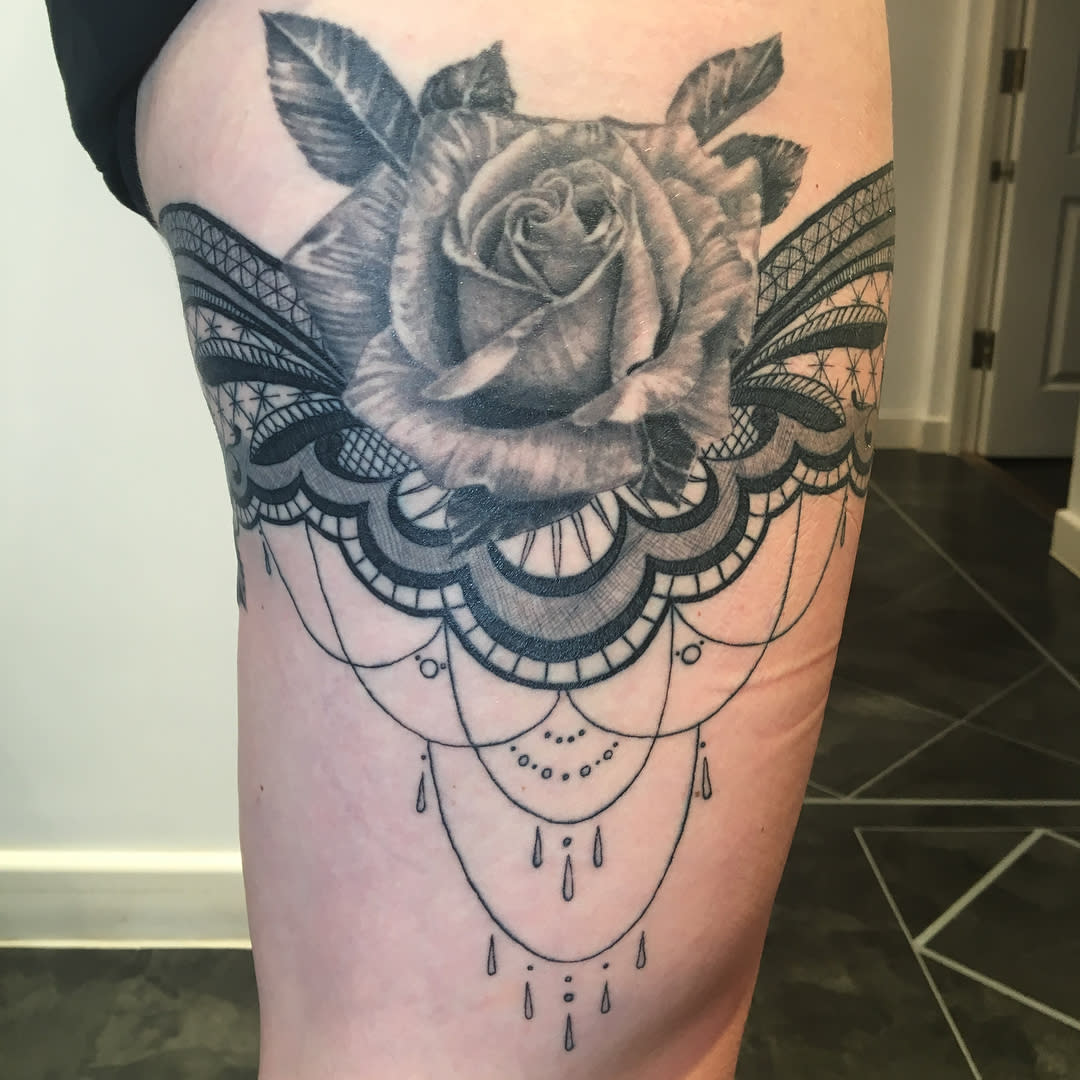 Tattoo on thigh of intricate black and gray rose with lace and bead designs hanging below