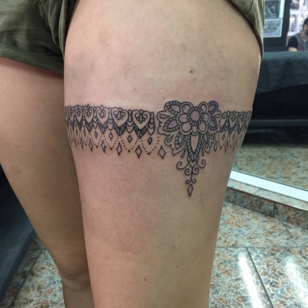 Thigh tattoo of intricate lace design with floral patterns and diamond-shaped details