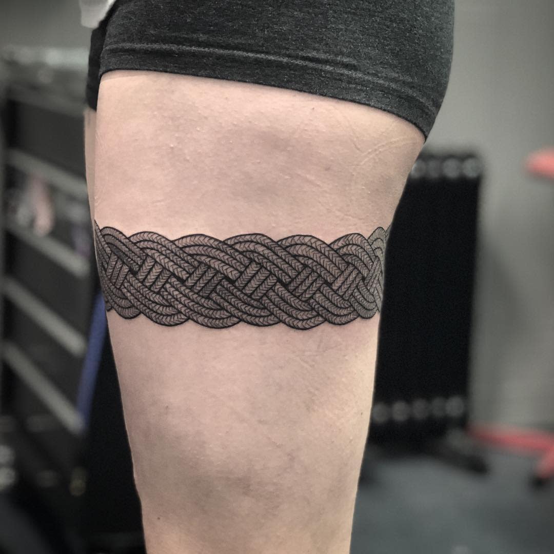Close-up of a leg with a detailed black Celtic knot tattoo wrapped around the upper thigh