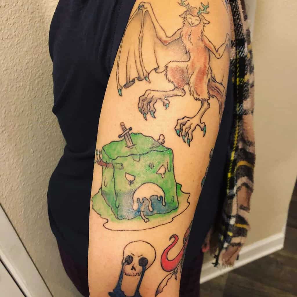 Whimsical arm tattoo featuring a gelatinous cube, a demon-like creature, and a skull, inspired by D&D monsters