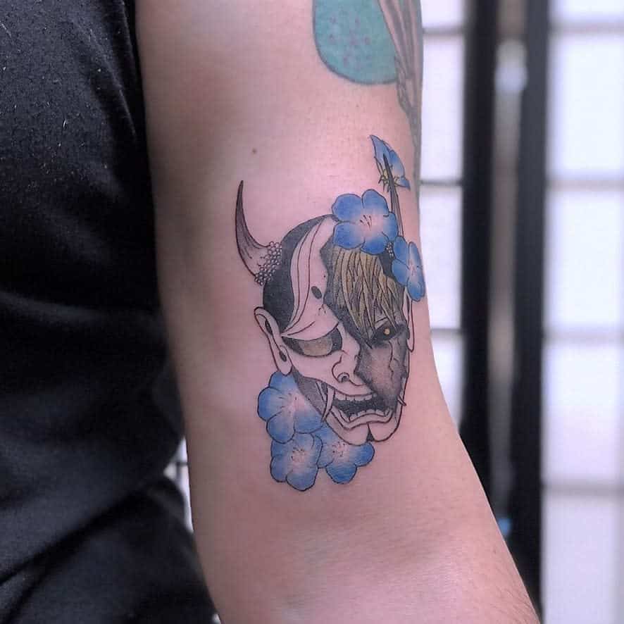 A detailed tattoo of Genos from One Punch Man fused with a half-demon mask, adorned with blue flowers for a striking contrast