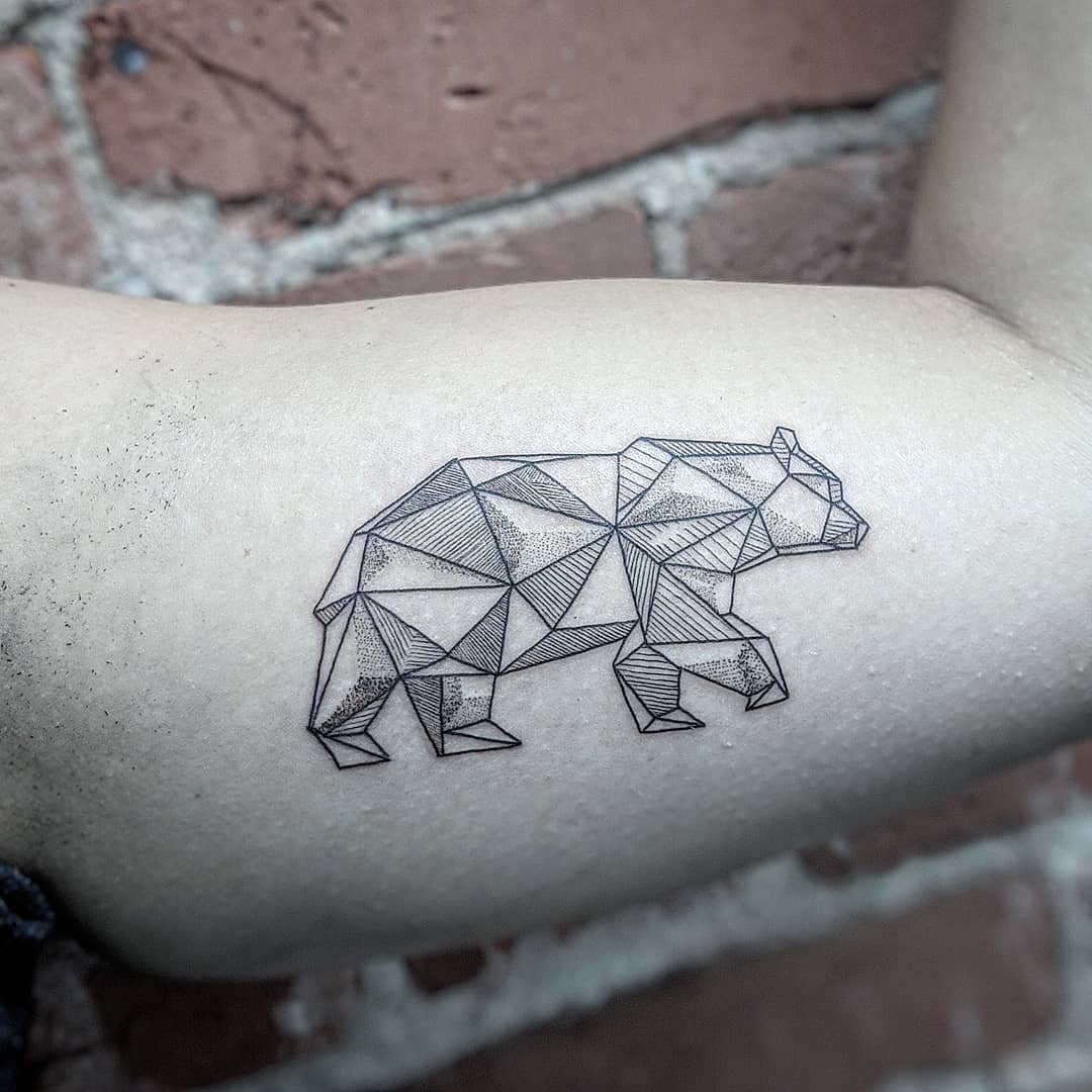 Geometric bear tattoo on bicep against a rugged brick wall background