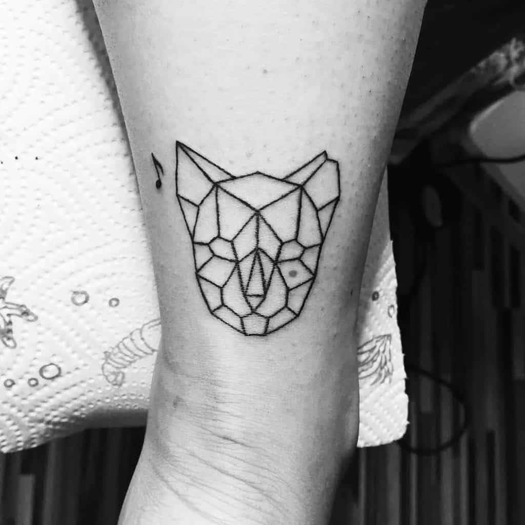 Geometric tattoo of a cat's face on leg with small music note adjacent