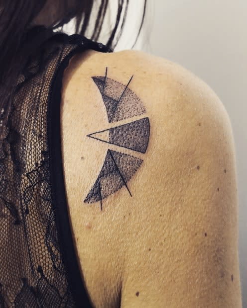 Geometric tattoo with shaded semi-circles and crescent moon designs intertwining lines on a person's upper back shoulder