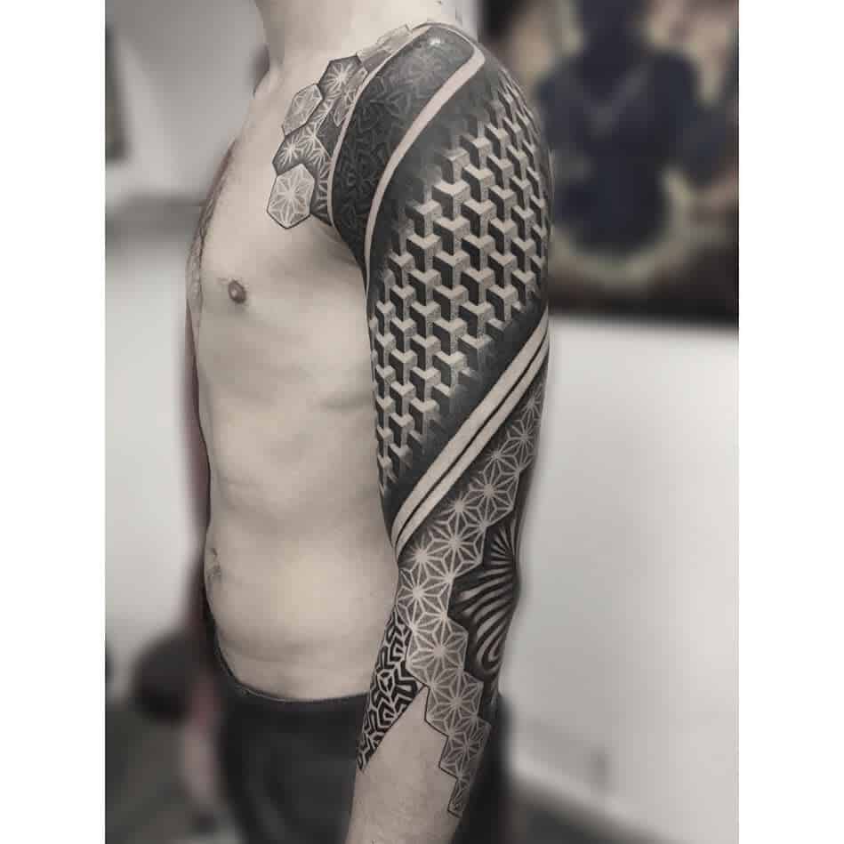 A black and grey full sleeve tattoo featuring bold geometric patterns, including 3D cube designs, hexagons, and intricate linework, wrapping around the arm and shoulder