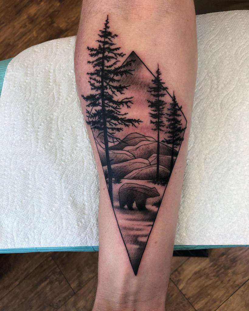 Tattoo of a bear with trees and mountains in a diamond shape on a forearm